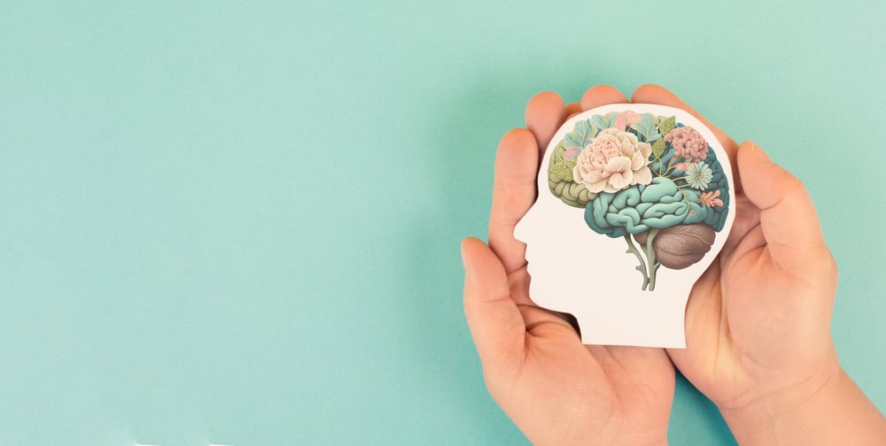 Hands holding paper head, human brain with flowers, self care and mental health concept